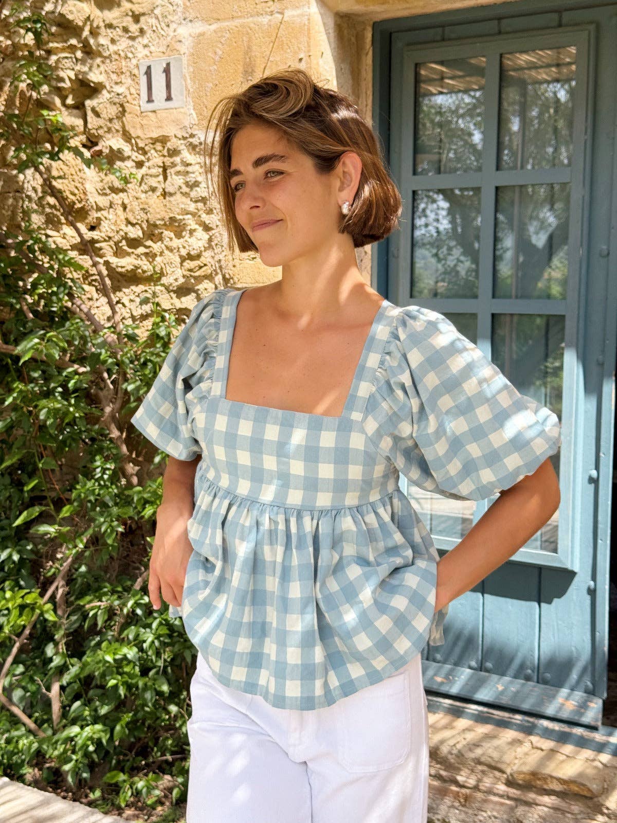 Modell i halvprofil forfra i blå gingham-bluse med firkantet utringning og puffermer – Vycora Archive