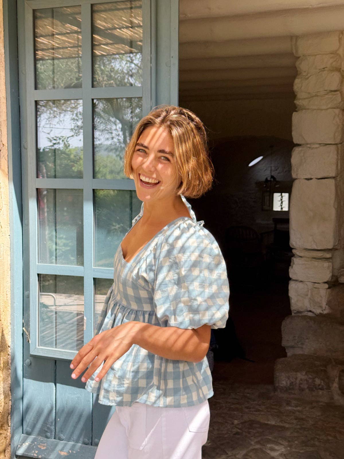 Poserende modell fra siden i skulpturell blå gingham-bluse med puffermer – Vycora