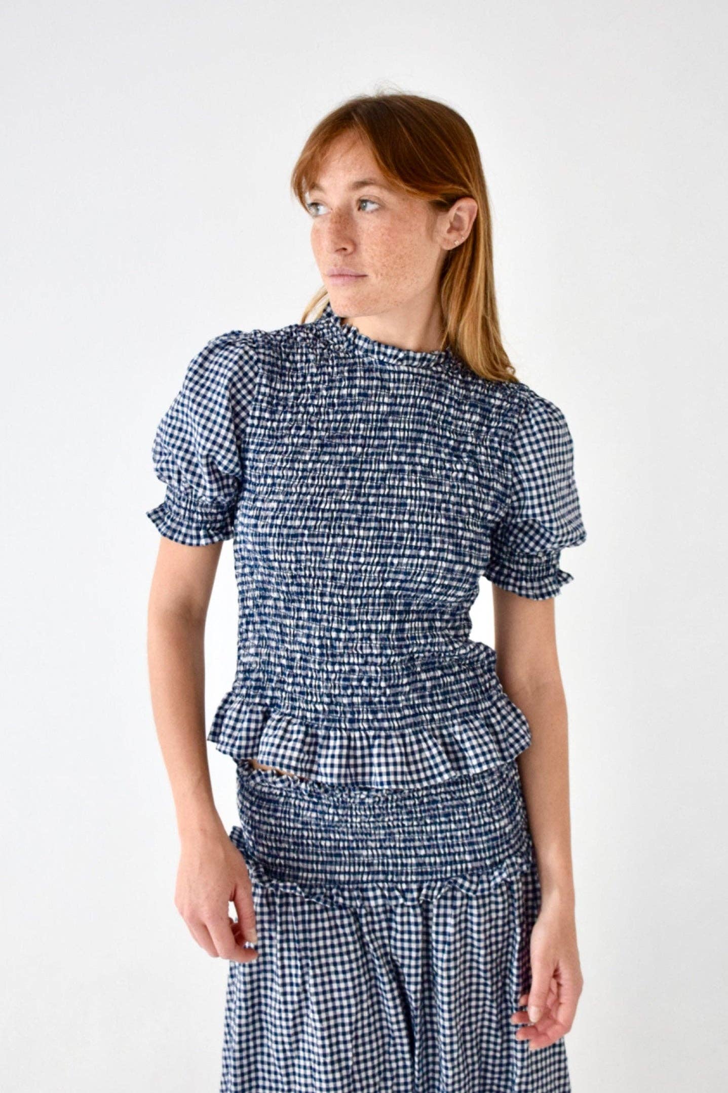 Modell i halvprofil forfra i kort marineblå gingham med puffermer og smocket livstykke – Vycora Archive